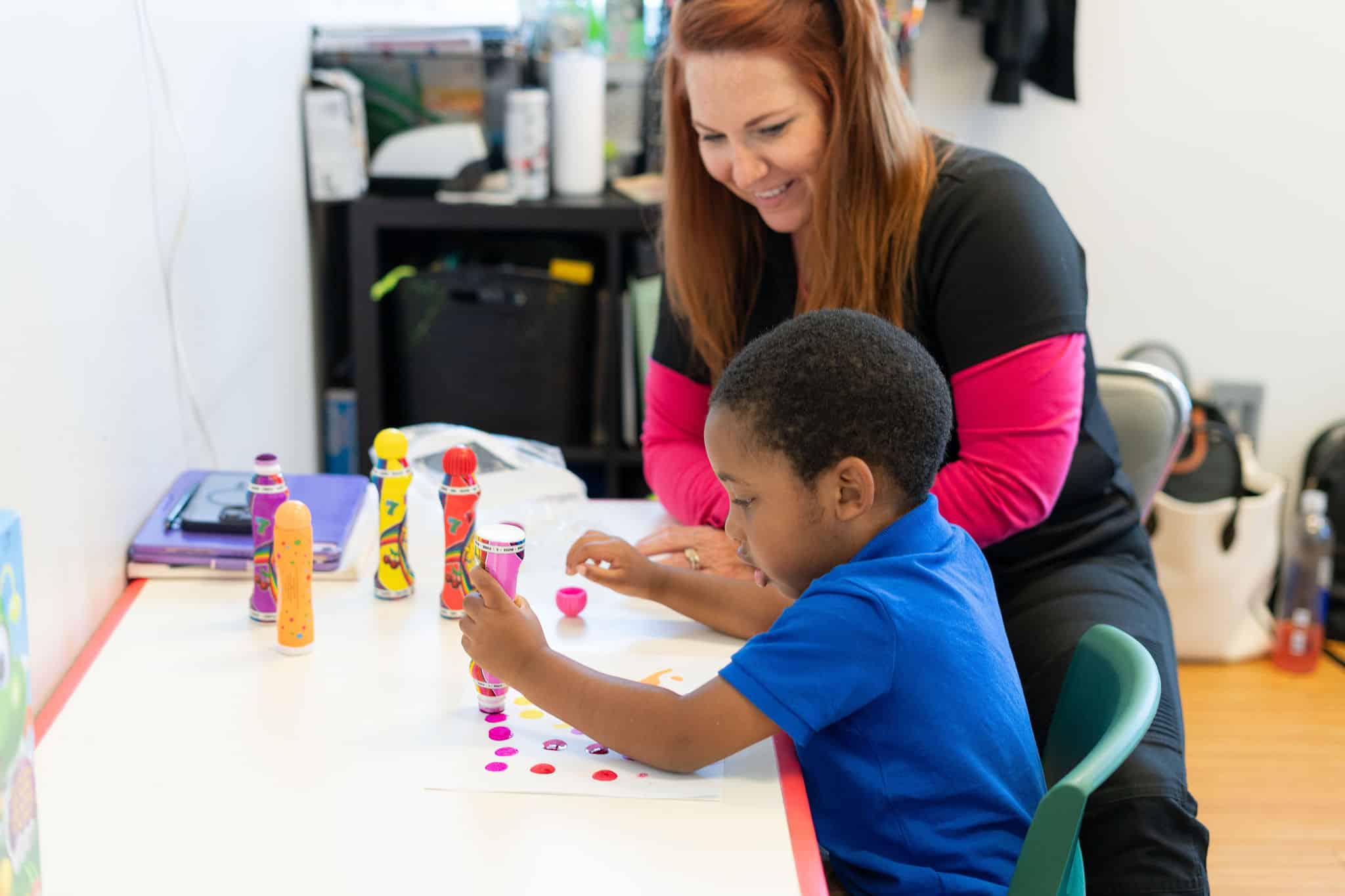 Child and therapist at table using dot markers to make picture